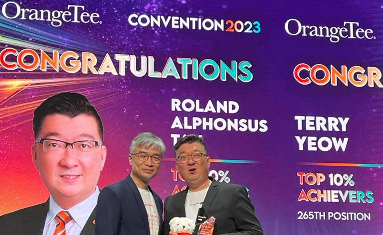 Alphonsus Roland Tan standing on stage at the OrangeTee Annual Achievers Awards 2023, for his achievements as a real estate agent in 2023.