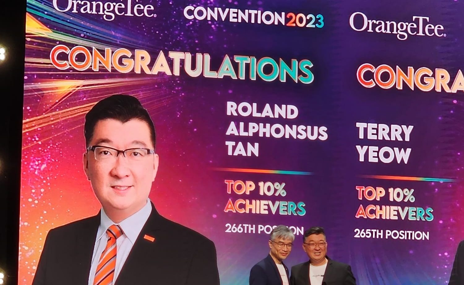 Alphonsus Roland Tan standing on stage at the OrangeTee Annual Achievers Awards 2023, for his achievements as a real estate agent in 2023.